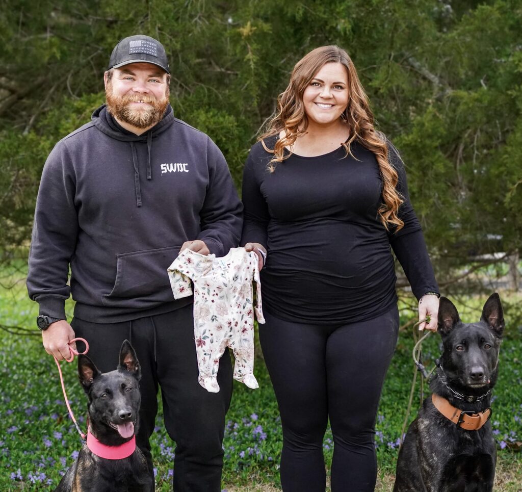 Lucas and Julianne from The Cultured Canine hold dog leashes and a baby onesie in a family photo birth announcement