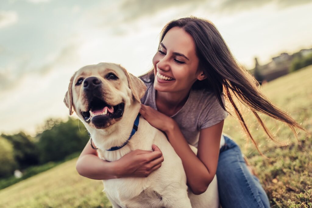 Smiling woman with happy yellow Labrador in a grassy field